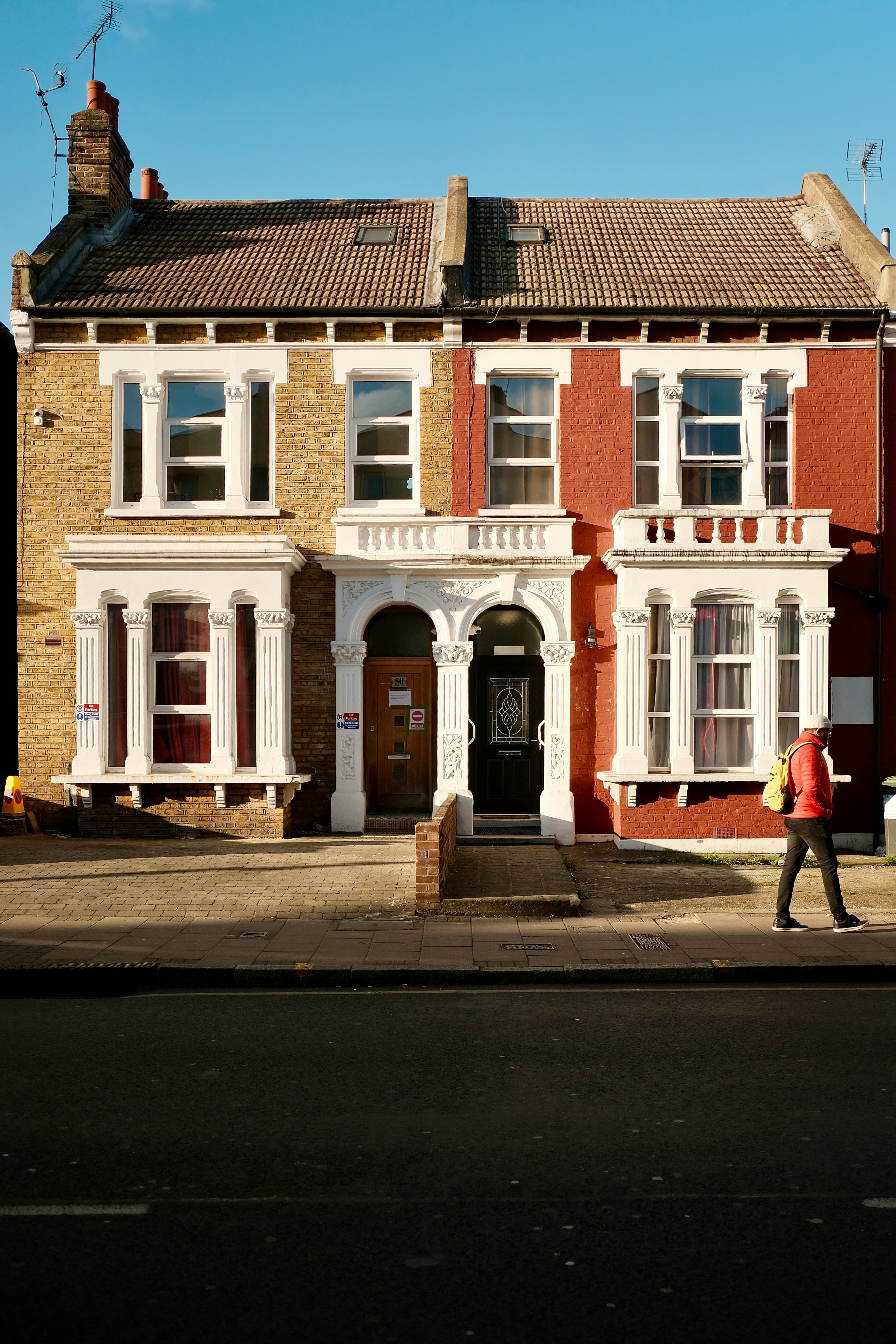 Person in red jacket walks past yellow and red brick houses with ornate white trim.